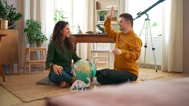 Young man with Down syndrome with his teacher using globe and learning about dinosaurs, homeschooling.