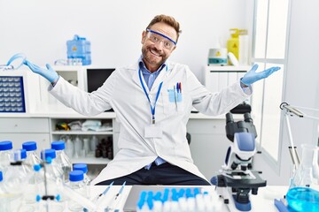 Middle age man working at scientist laboratory clueless and confused expression with arms and hands...