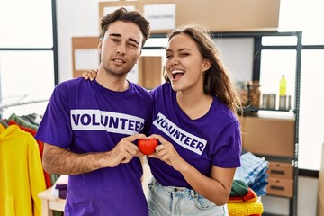 Young hispanic couple wearing volunteer t shirt holding heart winking looking at the camera with sexy expression, cheerful and happy face.
