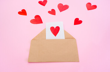 Paper envelope with a heart-shaped note inside and valentines hearts on a pink background. Flat lay, top view. Romantic love letter for Valentine's day concept.