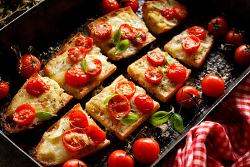 Baguette toasts with mozzarella cheese and cherry tomatoes seasoned with herbs in a baking tin, close up view