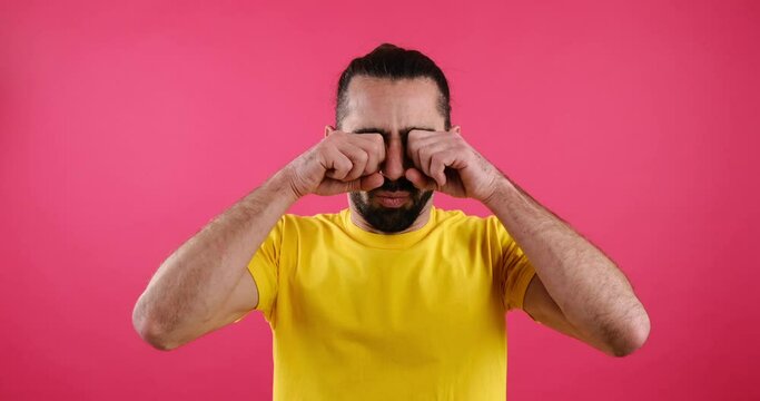 Shocked man rubbing his eyes in disbelief over pink background