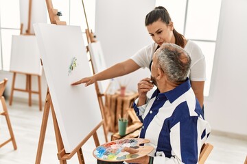 Young painting teacher woman teaching art to senior man painting on canvas at art studio