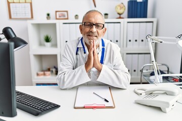 Mature doctor man at the clinic praying with hands together asking for forgiveness smiling confident.