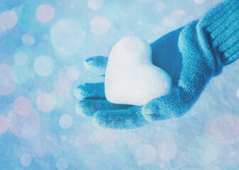 Female hand in the knitted glove with heart of snow on bokeh background. Love concept. Valentine day concept.
