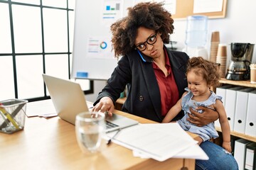 Young african american woman talking on the smartphone working with baby at office