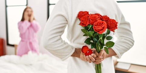 Man surprising his girlfriend with bouquet of roses at bedroom.