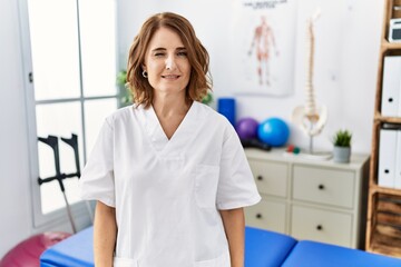 Fototapeta premium Middle age physiotherapist woman working at pain recovery clinic winking looking at the camera with sexy expression, cheerful and happy face.