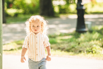Cute little boy with curly blonde hair playing in park
