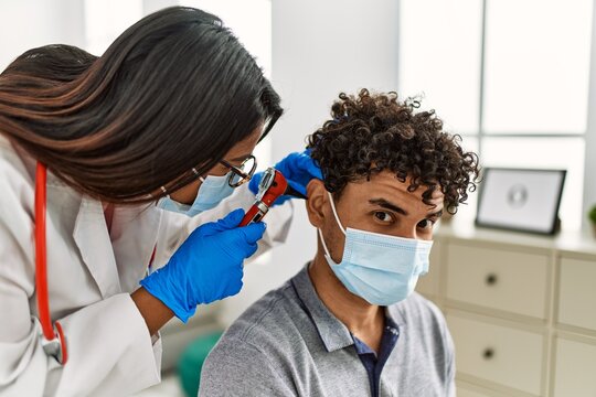 Young latin doctor woman auscultating the ear of man using otoscope at examination room.