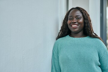 Young african woman smiling happy leaning on the wall