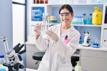 Young woman wearing scientist uniform holding test tubes with flowers at laboratory