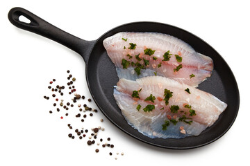 White fish fillet spilled with salt and chopped parsley lies on a cast-iron pan