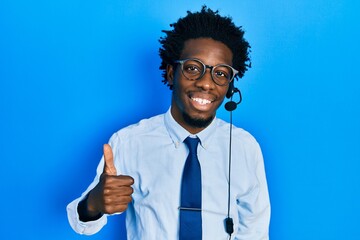 Young african american man wearing call center agent headset smiling happy and positive, thumb up doing excellent and approval sign