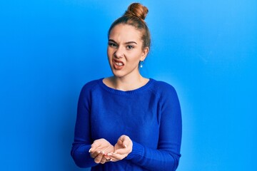 Young blonde woman holding hands together cupped, giving concept clueless and confused expression....