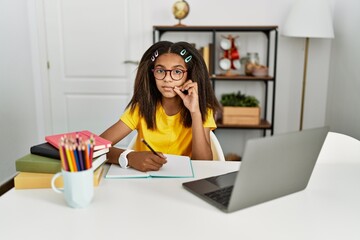 Young african american girl doing homework at home mouth and lips shut as zip with fingers. secret...