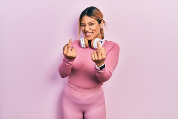 Beautiful hispanic woman wearing gym clothes and using headphones showing middle finger doing fuck...