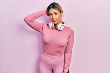 Beautiful hispanic woman wearing gym clothes and using headphones confuse and wondering about...