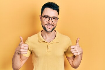 Young hispanic man wearing casual clothes and glasses success sign doing positive gesture with hand, thumbs up smiling and happy. cheerful expression and winner gesture.