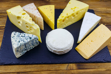Set of various types of cheese on black slate board on a wooden table