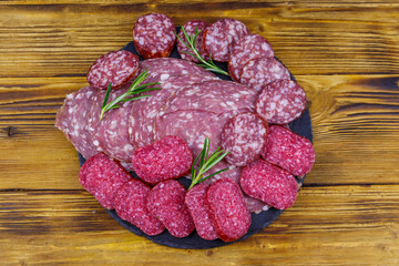 Different tasty sliced salami sausage on a black slate serving board on wooden table. Top view