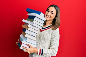 Young brunette student girl holding a pile of books smiling with a happy and cool smile on face. showing teeth.