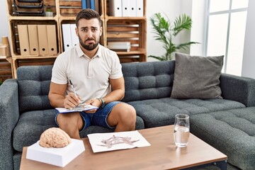 Fototapeta premium Handsome hispanic man working with rorschach test at psychology clinic depressed and worry for distress, crying angry and afraid. sad expression.
