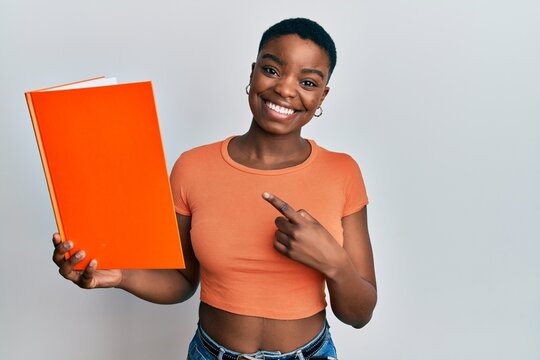 Young african american woman reading book smiling happy pointing with hand and finger