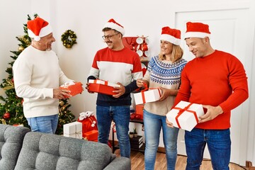 Group of middle age friends holding gifts standing by christmas tree at home.