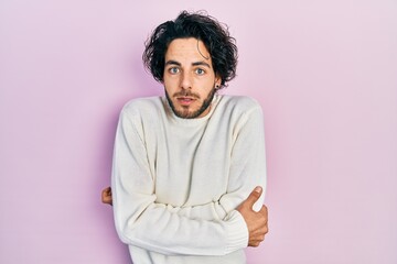 Handsome hispanic man wearing casual white sweater shaking and freezing for winter cold with sad and shock expression on face