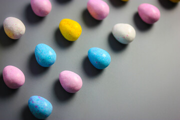 Multicolored bright Easter chocolate eggs yellow, white, pink, blue colors scattered on dark table background top view. Sweets and treats for children, kids in spring season holiday. Copy space