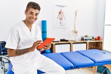 Young hispanic man working as physiotherapist using touchpad at physiotherapy room