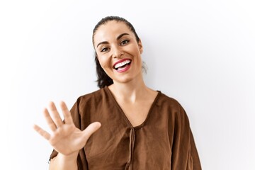 Young brunette woman standing over isolated background showing and pointing up with fingers number five while smiling confident and happy.