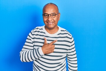 Middle age latin man wearing casual clothes and glasses cheerful with a smile on face pointing with hand and finger up to the side with happy and natural expression