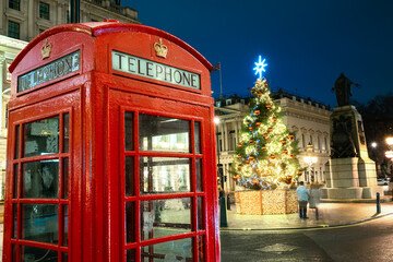 Christmas time in London: a red telephone booth in front of an illuminated Christmas Tree in Central London, UK, during night time