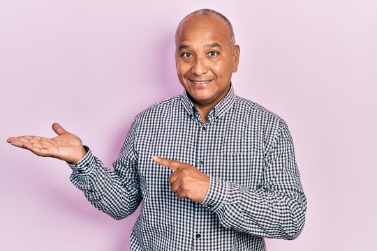 Middle age latin man wearing casual clothes amazed and smiling to the camera while presenting with hand and pointing with finger.