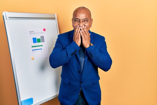 Middle age latin man wearing business clothes on chart presentation laughing and embarrassed giggle covering mouth with hands, gossip and scandal concept