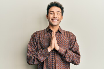 Handsome hispanic man wearing casual clothes praying with hands together asking for forgiveness smiling confident.