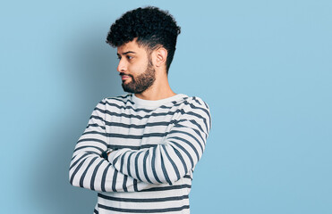 Obraz premium Young arab man with beard wearing casual striped sweater looking to the side with arms crossed convinced and confident