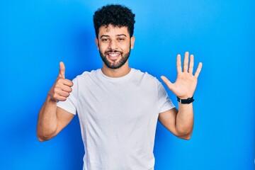 Naklejka premium Young arab man with beard wearing casual white t shirt showing and pointing up with fingers number six while smiling confident and happy.