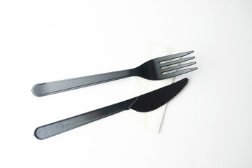 Clean plastic black forks and knives on white background. Disposable dishes, environmental pollution.