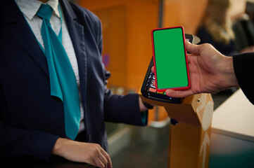 Close-up of male hand holding smartphone with green chroma key blank screen with copy space for mobile apps and advertising, near bank terminal while going through flight check-in board at airport