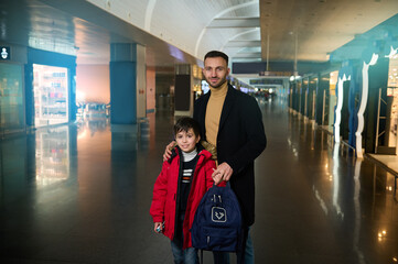 Handsome Caucasian man, young father travelling with his teenage son, standing together in the duty free shopping areas of the departure terminal of international airport