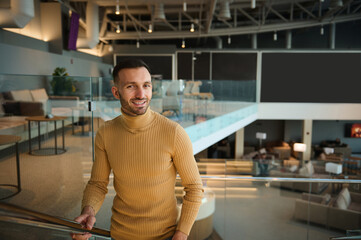 Attractive handsome middle-aged man in casual clothes climbs the stairs in the lounge of the departure terminal at the international airport while waiting for a flight. Businessman on a business trip