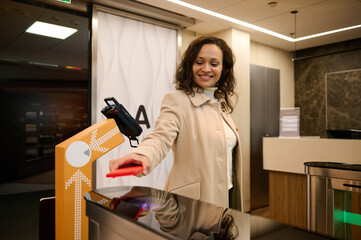 Business woman passenger scans information on the phone by placing it over the scanner to read the QR-codes at the check-in counter while entering the VIP lounge in the airport departure terminal