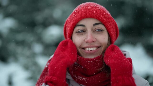 super close up happy smiling woman in knitted hat and scarf in snowy winter park at frizzy day with snowflakes. woman exhales steam, snowflakes on her face. Happy winter time, having fun