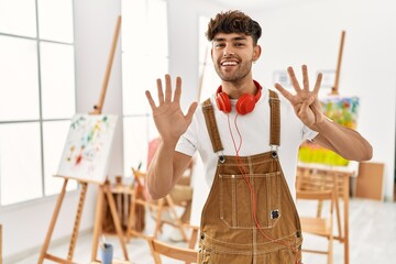 Young hispanic man at art studio showing and pointing up with fingers number nine while smiling...