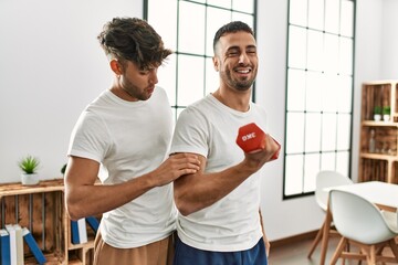 Two hispanic men couple smiling confident training using dumbbell at home