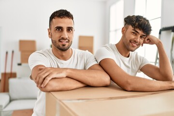 Obraz premium Two hispanic men couple smiling confident leaning on cardboard box at new home