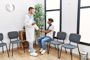 Two hispanic men doctor and patient shake hands at hospital waiting room